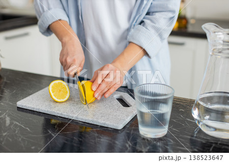 Hands slicing fresh lemon for water in home kitchen preparing healthy detox drink closeup shot 138523647