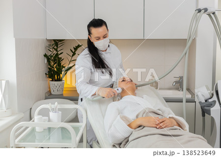 Beautician makes woman RF lifting cosmetology procedure of face and cheek area, collagen mask at spa 138523649