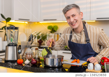 Middle-aged man preparing healthy diet soup in kitchen smiling during homemade meal routine at home 138523650