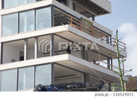 Construction workers installing materials on multi-storey residential building using crane. Urban development and building process concept. Construction workers installing materials on multi-storey residential building using crane. Urban development and building process concept. 138524915