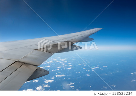 Airplane wing cutting across a vast blue sky dotted with fluffy clouds, conveying flight, travel and freedom from a high altitude window perspective over the horizon Airplane wing cutting across a vast blue sky dotted with fluffy clouds, conveying flight, travel and freedom from a high altitude window perspective over the horizon 138525234