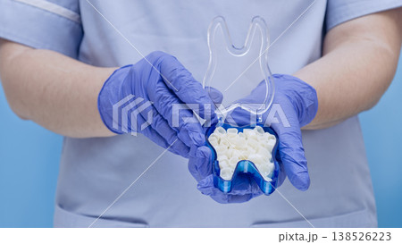 Dentist in blue gloves holding a tooth-shaped box with temporary dental crowns. Dentist in blue gloves holding a tooth-shaped box with temporary dental crowns. 138526223