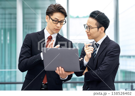 オフィスビルでノートパソコンを見ながら打ち合わせをする二人の日本人ビジネスマン オフィスビルでノートパソコンを見ながら打ち合わせをする二人の日本人ビジネスマン 138526402