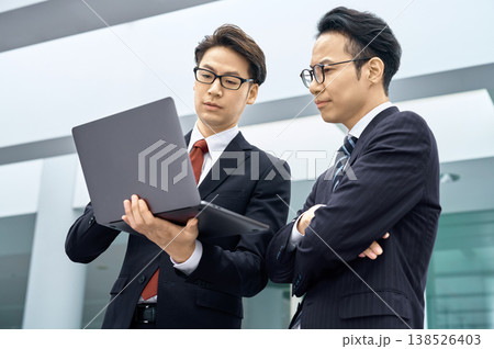 ノートパソコンを囲んで屋外で打ち合わせをするスーツ姿の日本人ビジネスマン2人 138526403