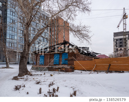 Old wooden house with shutters against modern high rise buildings covered in snow cold early spring urban contrast cityscape and winter atmosphere. Old wooden house with shutters against modern high rise buildings covered in snow cold early spring urban contrast cityscape and winter atmosphere. 138526579