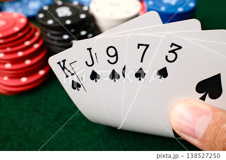 Hand holding Flush combination poker playing cards with colorful casino chips on green felt table gambling Hand holding Flush combination poker playing cards with colorful casino chips on green felt table gambling 138527250