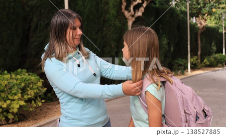 Mother in casual hoodie engages in conversation with daughter carrying school backpack outside school entrance. Mother in casual hoodie engages in conversation with daughter carrying school backpack outside school entrance. 138527885