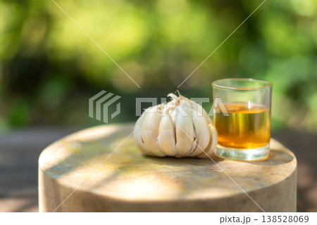 Fresh Garlic Bulb and Glass of Herbal Oil on Rustic Wooden Board 138528069