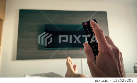 First person view of a man relaxing in hotel bed with remote control facing television. Turning on TV 138529205