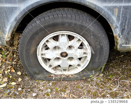 A rusted vintage car being abandoned on a street with flat tires and rusty bodywork 138529668