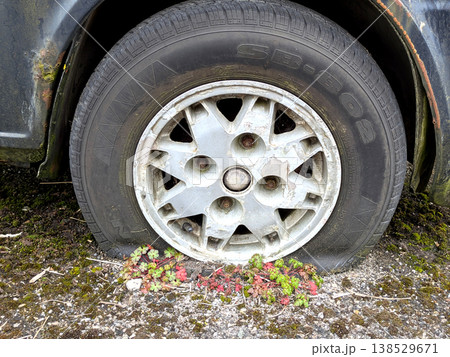 A rusted vintage car being abandoned on a street with flat tires and rusty bodywork 138529671