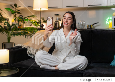 Young woman on smartphone video call waves hello laughs shares news smiling chat with friend evening 138530061