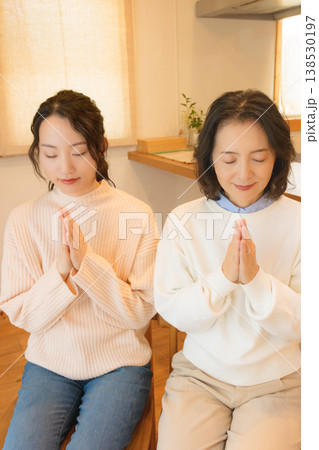 自宅で故人に祈りを捧げる母と娘 自宅で故人に祈りを捧げる母と娘 138530197