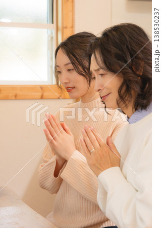 自宅で故人に祈りを捧げる母と娘 138530237