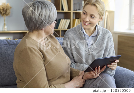 Caregiver supporting senior woman with tablet while chatting together on home sofa Caregiver supporting senior woman with tablet while chatting together on home sofa 138530509