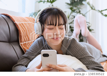ヘッドホンでスマートフォンを楽しむ女性 リビングでくつろぐライフスタイル ヘッドホンでスマートフォンを楽しむ女性 リビングでくつろぐライフスタイル 138530522