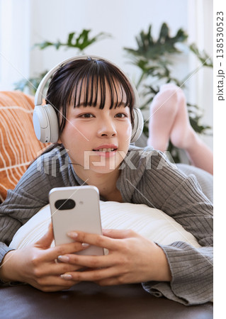 ヘッドホンでスマートフォンを楽しむ女性 リビングでくつろぐライフスタイル ヘッドホンでスマートフォンを楽しむ女性 リビングでくつろぐライフスタイル 138530523