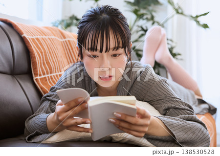ソファで寝転び本を読む女性 自宅でくつろぐ読書の時間 ソファで寝転び本を読む女性 自宅でくつろぐ読書の時間 138530528