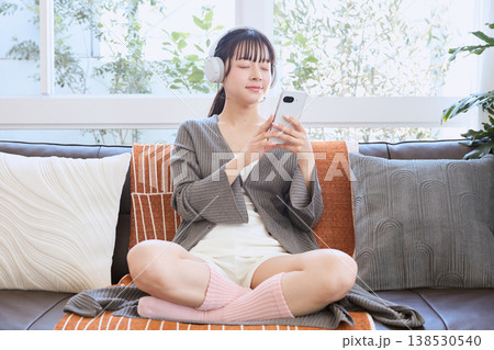 ヘッドホンでスマートフォンを使う女性 自宅で楽しむライフスタイル ヘッドホンでスマートフォンを使う女性 自宅で楽しむライフスタイル 138530540