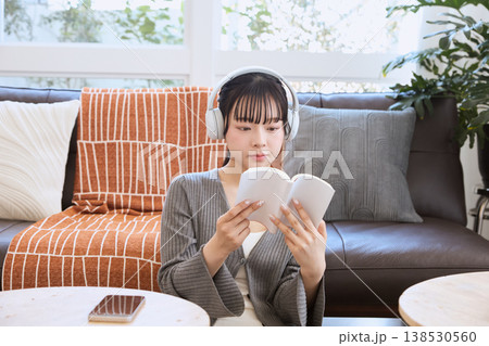 ヘッドホンで音楽を聴きながら本を読む女性 自宅で過ごすリラックスタイム ヘッドホンで音楽を聴きながら本を読む女性 自宅で過ごすリラックスタイム 138530560