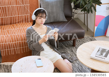ヘッドホンで音楽を聴きながら本を読む女性　自宅で過ごすリラックスタイム 138530565