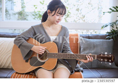 自宅のリビングでアコースティックギターを弾く若い女性 138530597