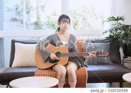 自宅のリビングでアコースティックギターを弾く若い女性 138530599