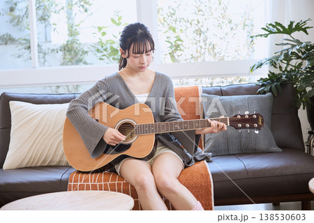 自宅のリビングでアコースティックギターを弾く若い女性 138530603