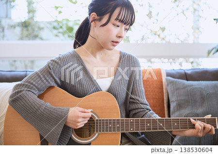 自宅でアコースティックギターを弾く若い女性 138530604