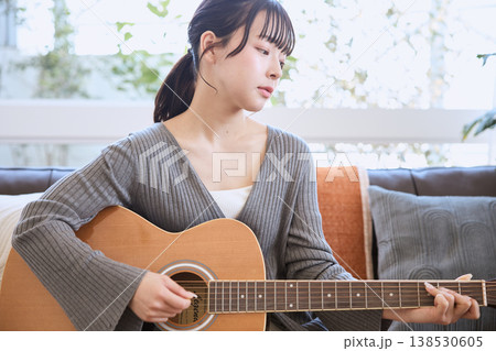 自宅でアコースティックギターを弾く若い女性 138530605