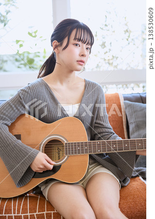 自宅でアコースティックギターを弾く若い女性 138530609