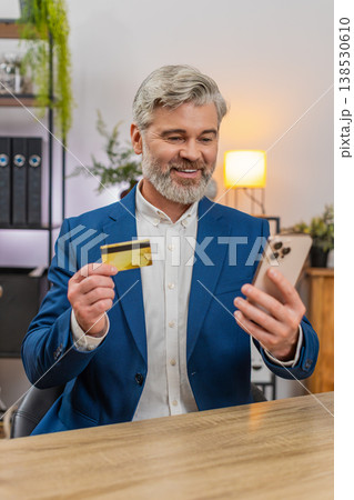 Middle-aged businessman confirms payment on smartphone holding credit card smiling at smooth service Middle-aged businessman confirms payment on smartphone holding credit card smiling at smooth service 138530610