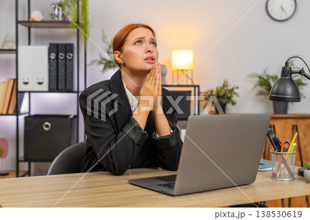 Young businesswoman folds hands praying before laptop looking up hoping project approval and order 138530619