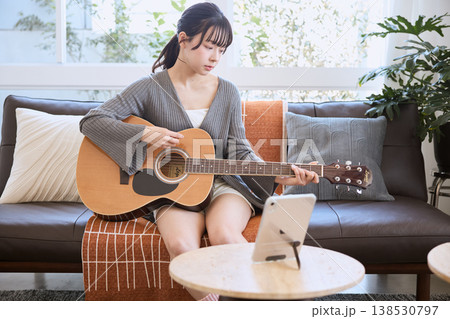 タブレットを見ながらアコースティックギターを弾く若い女性 タブレットを見ながらアコースティックギターを弾く若い女性 138530797