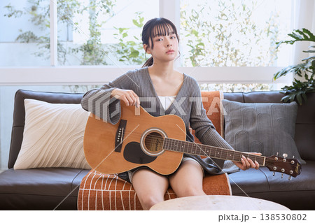 自宅のリビングでアコースティックギターを持つ若い女性 138530802