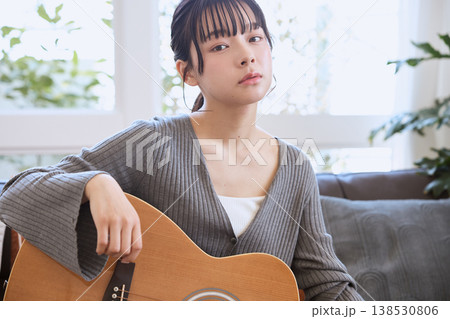 自宅のリビングでアコースティックギターを持つ若い女性 自宅のリビングでアコースティックギターを持つ若い女性 138530806