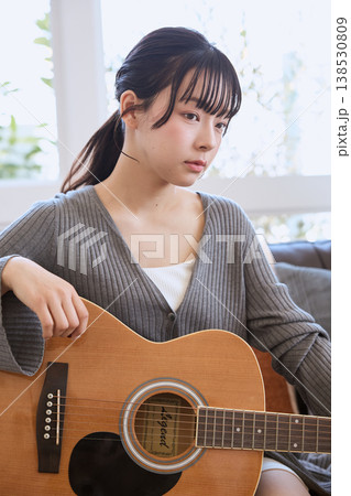 自宅のリビングでアコースティックギターを持つ若い女性 138530809