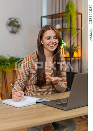 Young woman in headphones on video call gestures and writes notes in notebook while focused on work Young woman in headphones on video call gestures and writes notes in notebook while focused on work 138531080