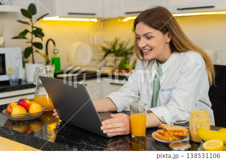 Middle-aged woman cheering at laptop in kitchen after online win during healthy breakfast at home Middle-aged woman cheering at laptop in kitchen after online win during healthy breakfast at home 138531106