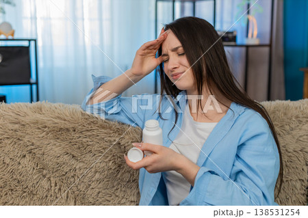 Woman suffering severe headache sitting holding head exhausted searching taking pain relief pills 138531254