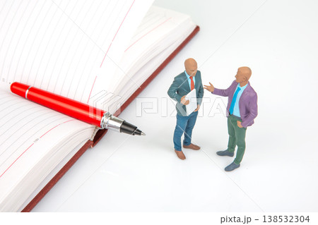 Miniature people talking near an open notebook and a red pen at a workspace setting Miniature people talking near an open notebook and a red pen at a workspace setting 138532304