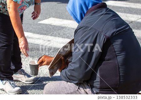 Person giving coins to individual sitting on street in city during daylight hours Person giving coins to individual sitting on street in city during daylight hours 138532333