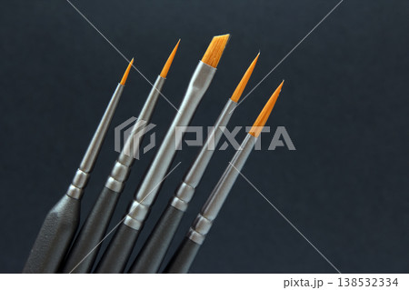 Brushes are lined up on a dark surface showing different sizes and shapes for painting or artwork 138532334
