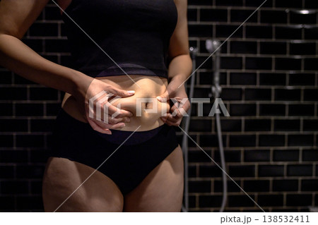 少し太ったお腹の贅肉をつまむ若い女性 太り始め お風呂 太った部分円形強調 少し太ったお腹の贅肉をつまむ若い女性 太り始め お風呂 太った部分円形強調 138532411