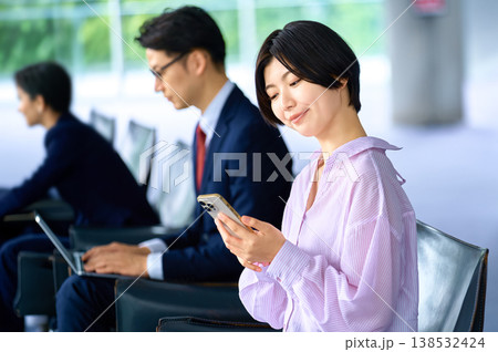 オフィスや空港のロビーでスマホを操作する笑顔の日本人女性 138532424