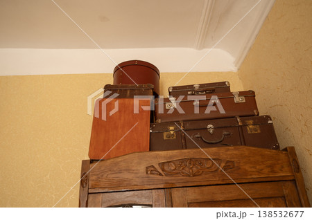 Vintage suitcases and a round hat box stacked on top of a wooden wardrobe 138532677