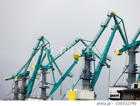 Industrial port cranes against cloudy sky, heavy machinery for cargo handling and shipping logistics, maritime infrastructure with steel structures and loading equipment in harbor environment 138532740