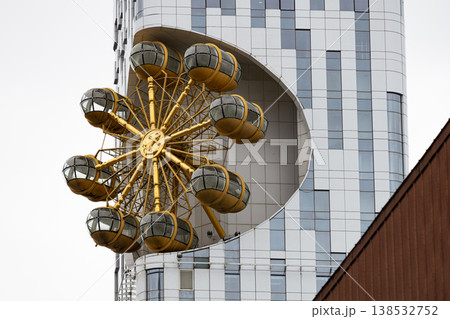 Modern building facade with golden ferris wheel structure and glass capsules, futuristic urban architecture detail, observation attraction integrated into high rise city design concept 138532752