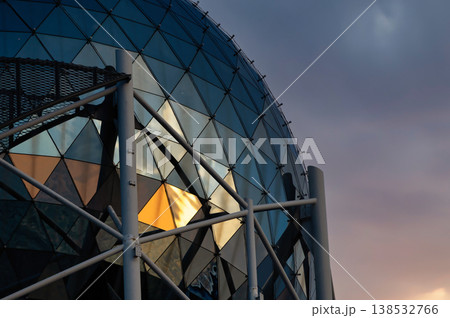 Modern glass dome architecture with geometric triangular panels and steel structure, futuristic building exterior reflecting warm sunset light, abstract urban design, minimal composition with copy spa 138532766