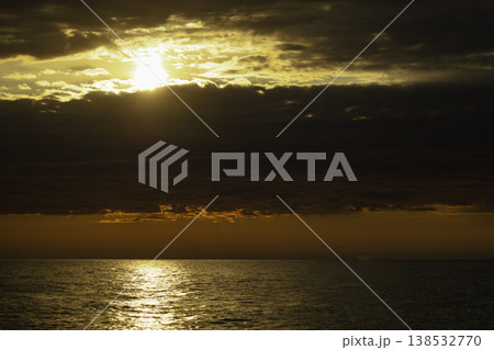 Golden sunset over calm sea with dramatic clouds and sun rays breaking through sky, warm orange horizon, tranquil ocean surface, atmospheric seascape, natural light, serene evening landscape Golden sunset over calm sea with dramatic clouds and sun rays breaking through sky, warm orange horizon, tranquil ocean surface, atmospheric seascape, natural light, serene evening landscape 138532770
